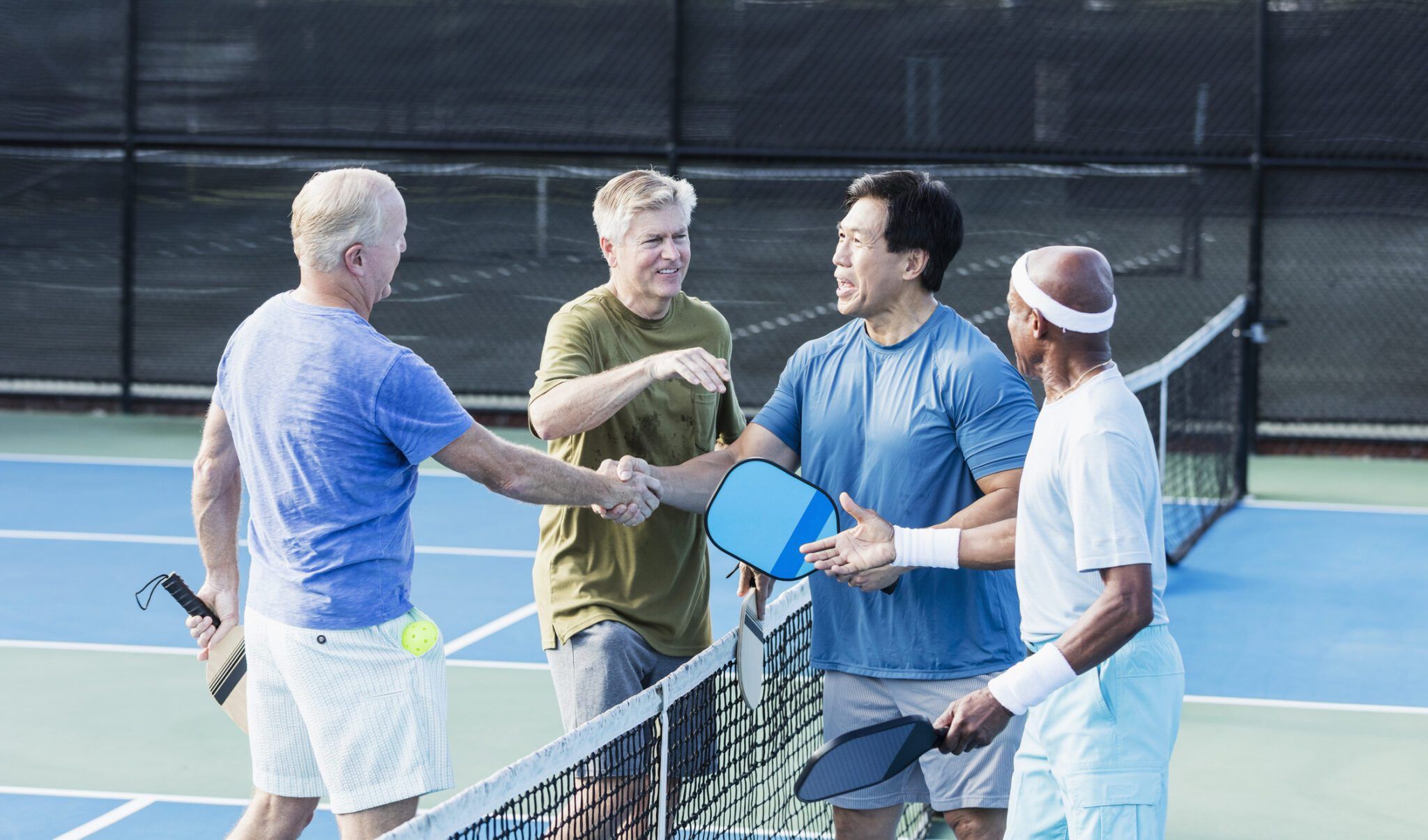Group of senior men shaking hands on pickleball court